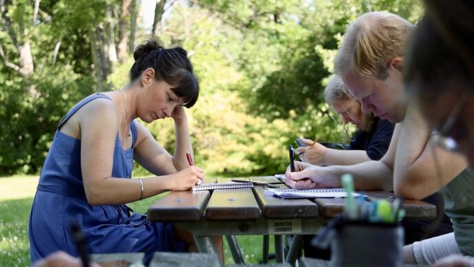 Tre personer sitter vid ett bord i solen och skriver.