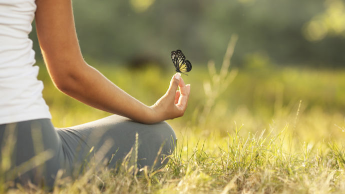 En människa sitter ute och mediterar och har en fjäril på handen